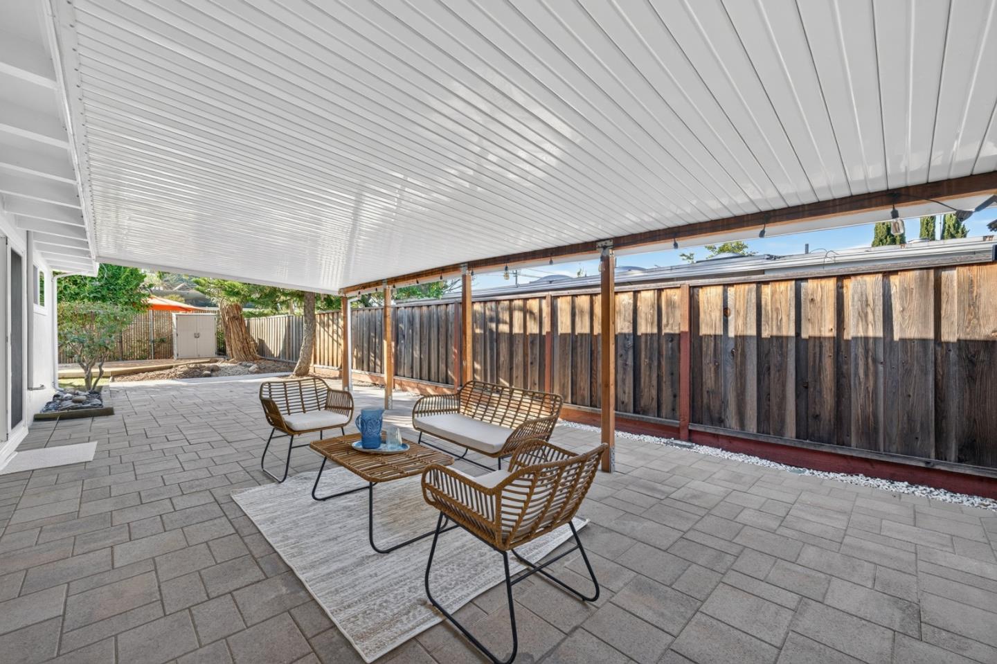Covered backyard patio with gray pavers, a white ceiling, and woven seating.