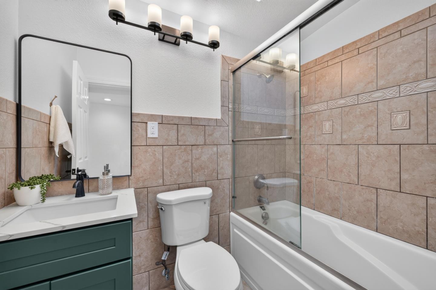 Bathroom with tan tile, a glass-screened bathtub, and a dark green vanity.