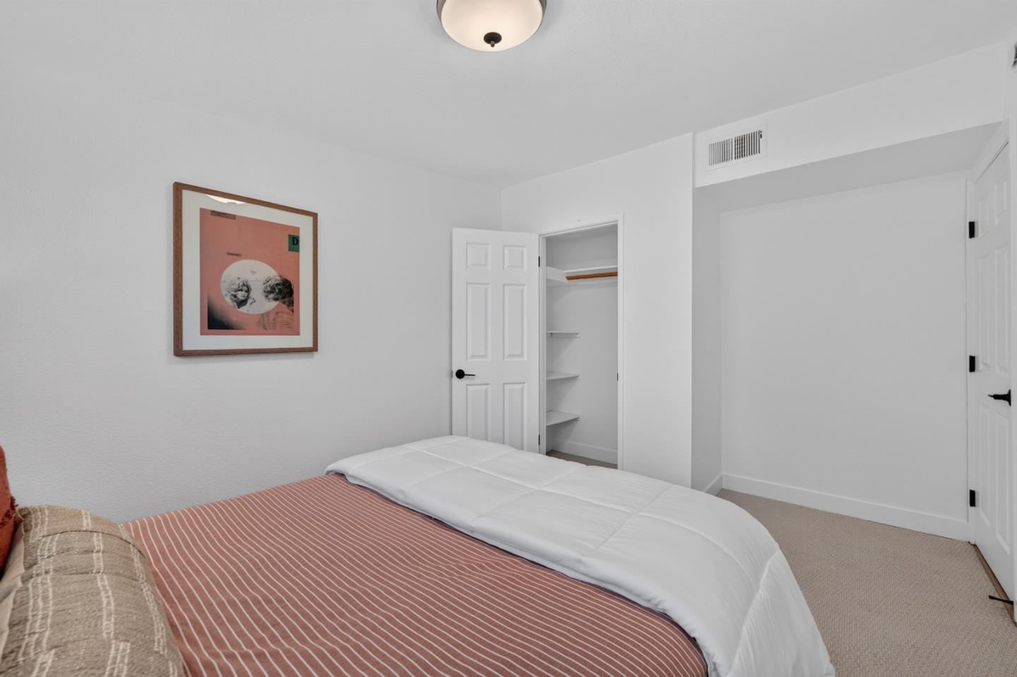 Bedroom with a red striped bedspread, white duvet, and open closet.