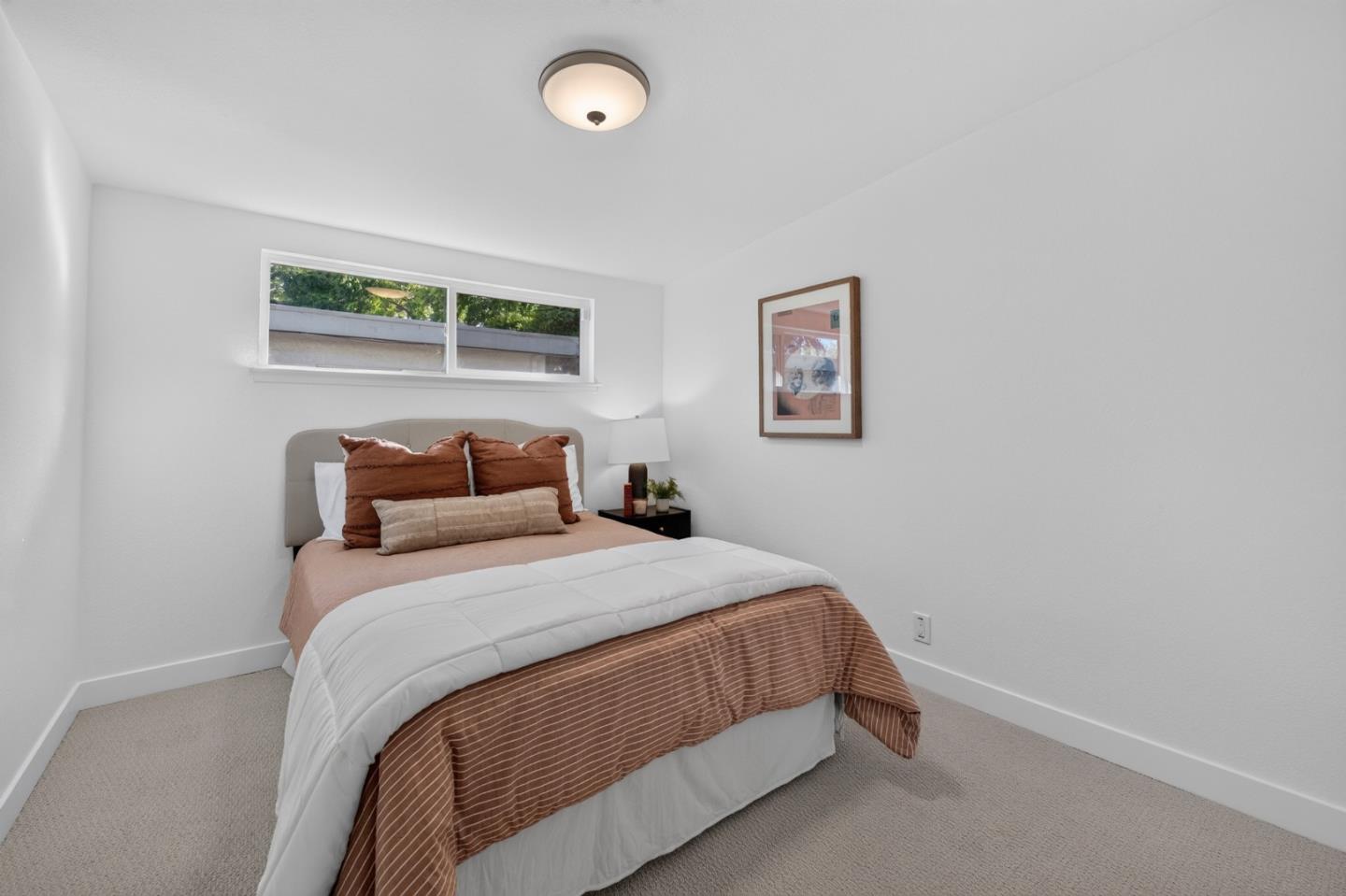 Staged bedroom with rust-colored bedding, a narrow window above the bed, and framed wall art.