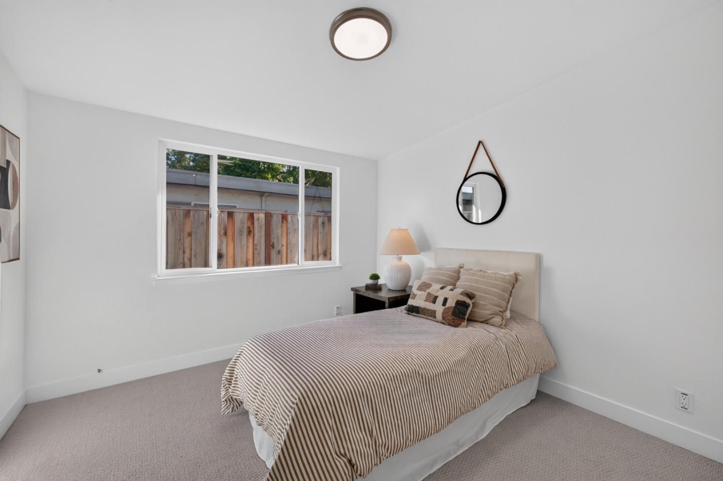 Staged bedroom with a striped bedspread and a large window overlooking a wooden fence.