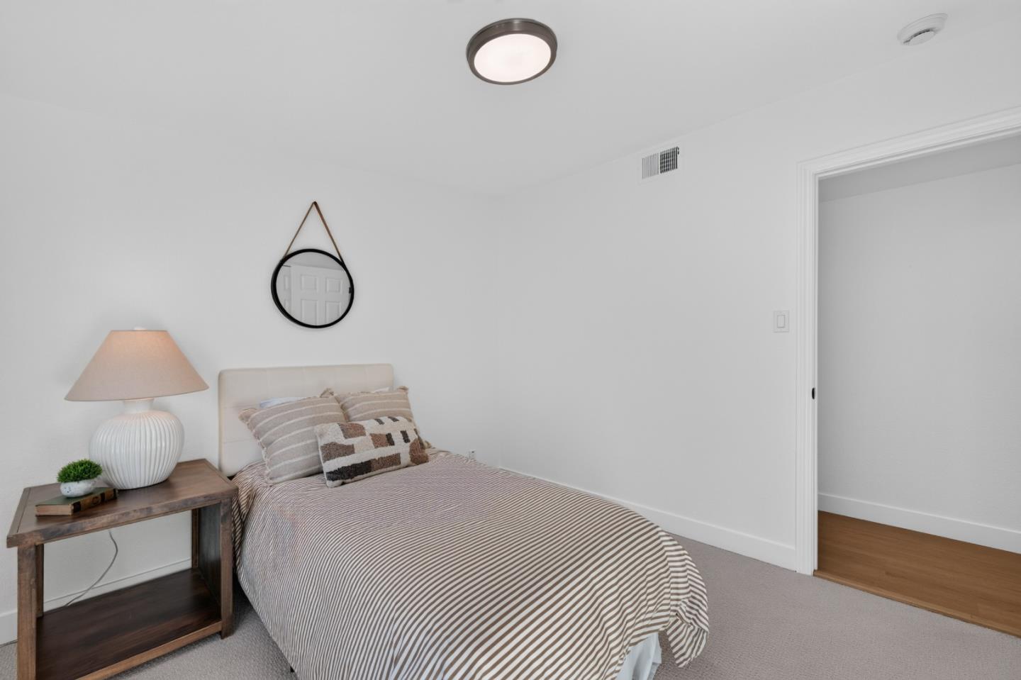Staged bedroom with striped bedding, a wooden bedside table, and a round mirror above the bed.