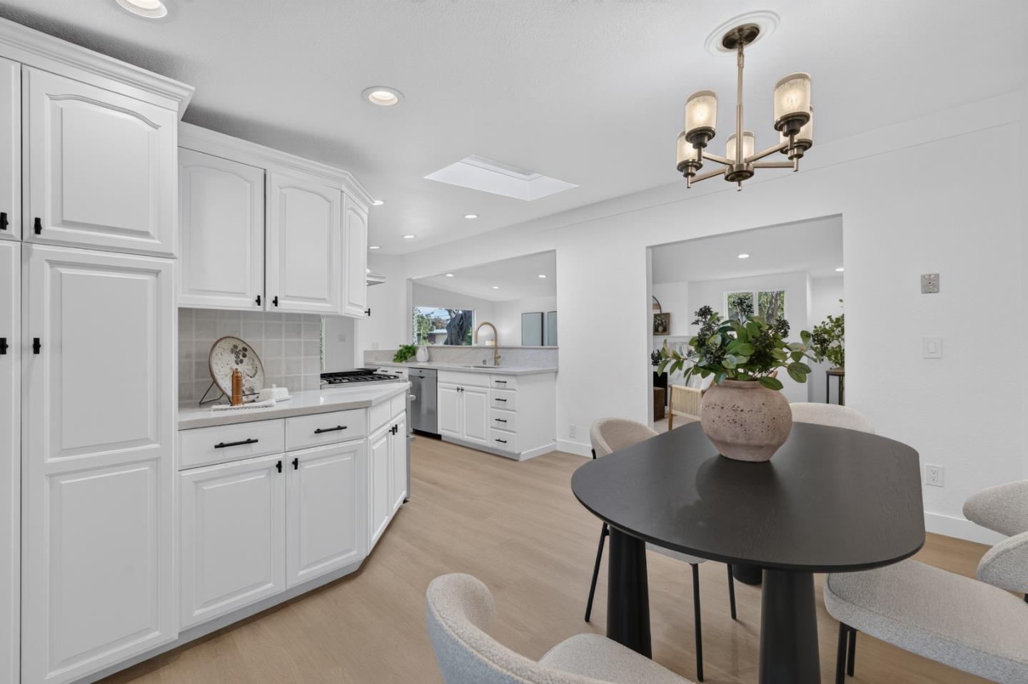 Bright kitchen and dining area with white cabinetry, light wood floors, and a black oval table.