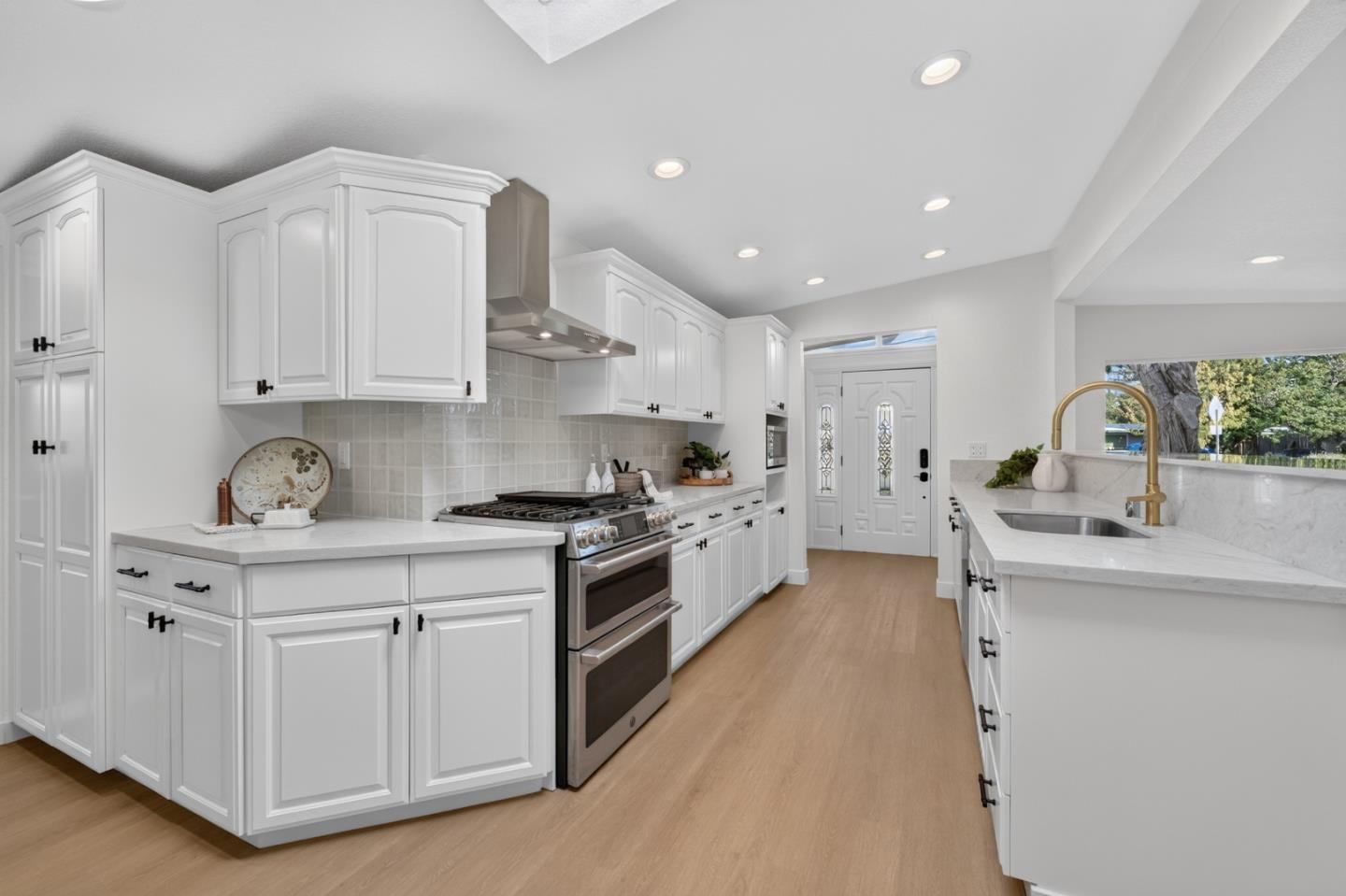 Bright white kitchen with a stainless steel range, stone counters, and brass sink faucet.
