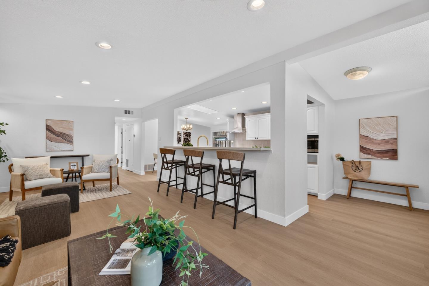 Open-plan living room and kitchen with a breakfast bar, white cabinetry, and neutral furnishings.