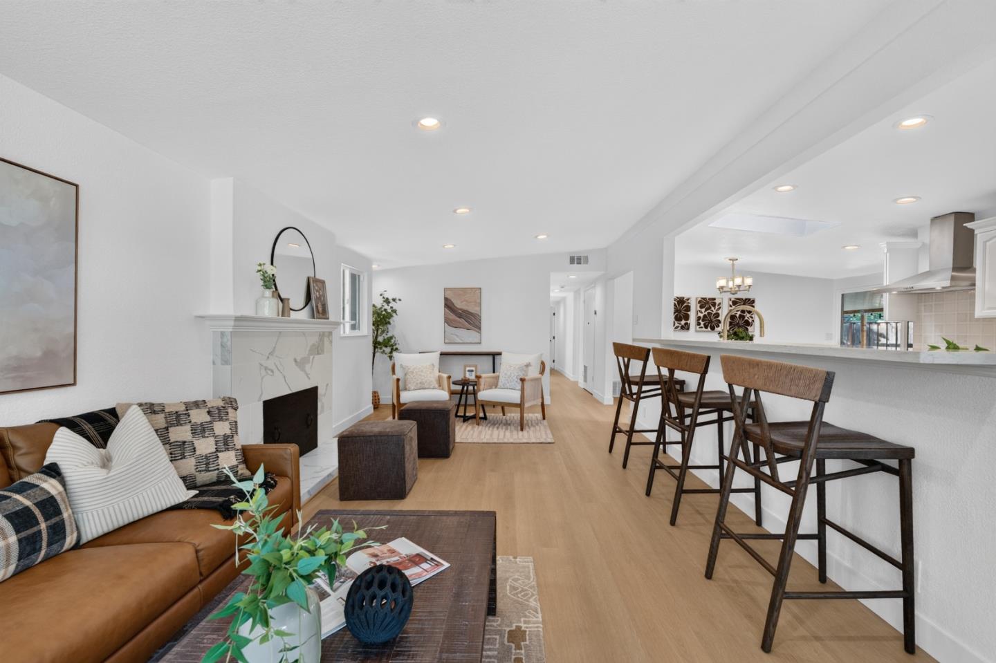 Open-plan living room with a leather sofa, marble fireplace, and kitchen island with bar seating.