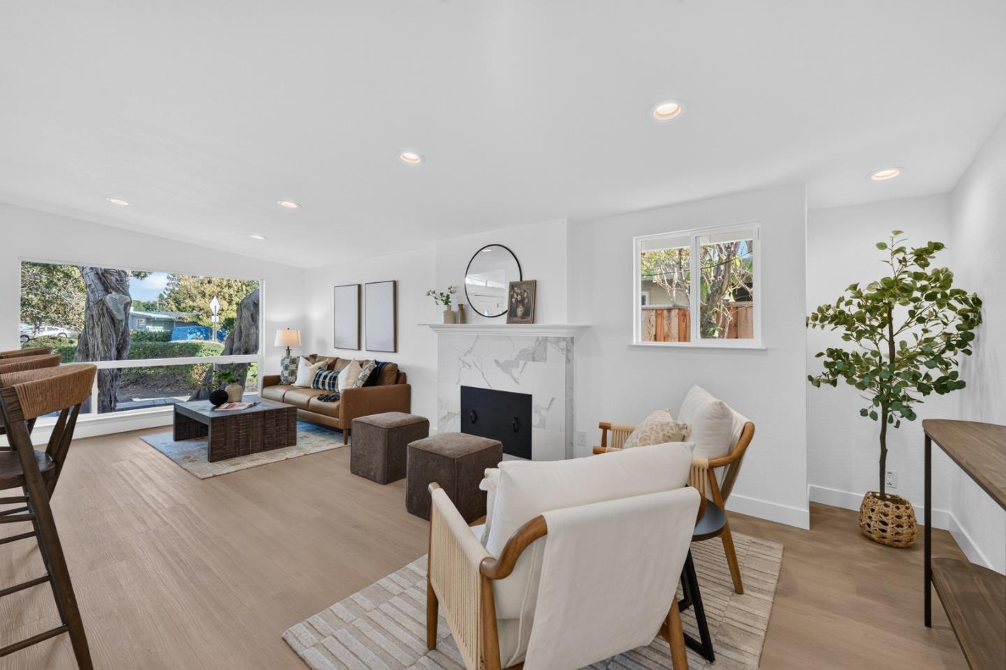 Staged living room with a marble-look fireplace and wide picture window overlooking trees.