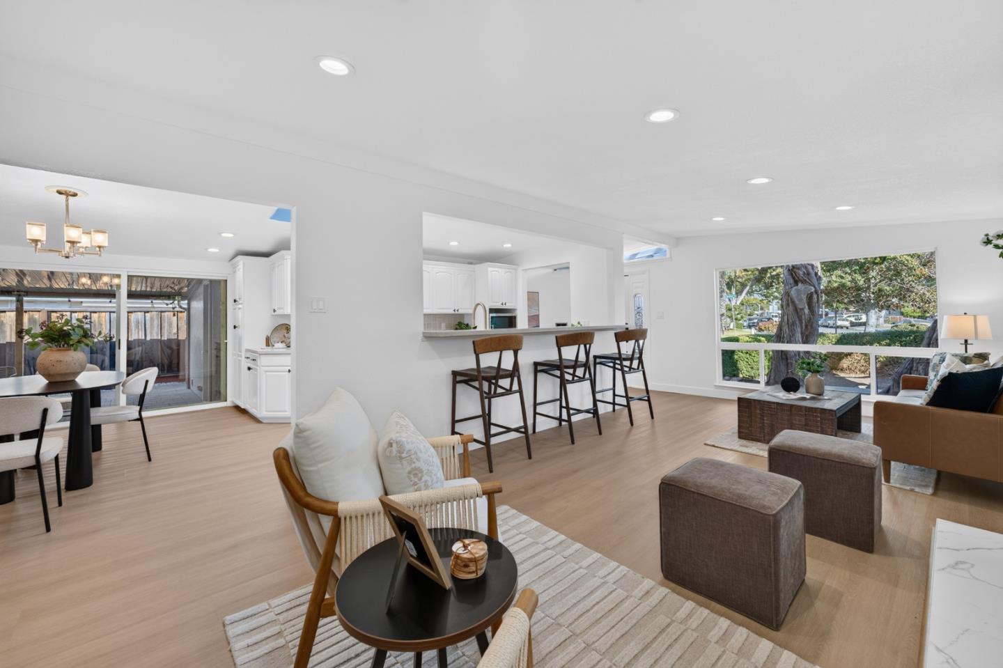 Open-plan living and dining room with a white kitchen, breakfast bar, and large windows overlooking trees.