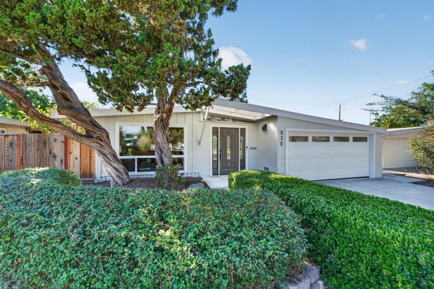 Single-story home with a sloping roof, white garage door, and mature trees in front.