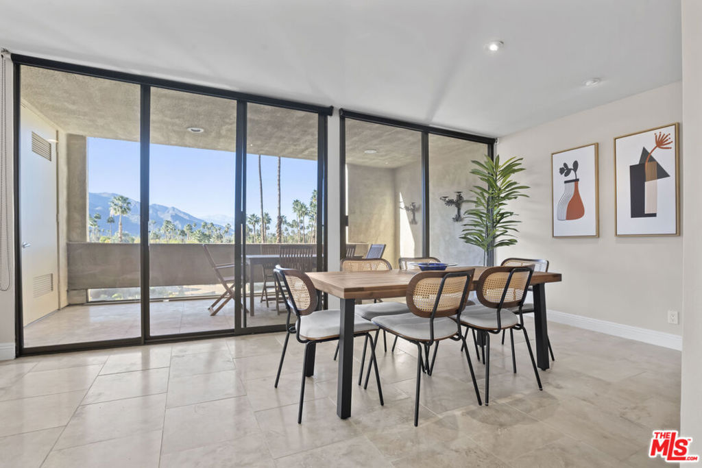 Dining room with a wood table, sliding glass doors, and views of palm trees and mountains.