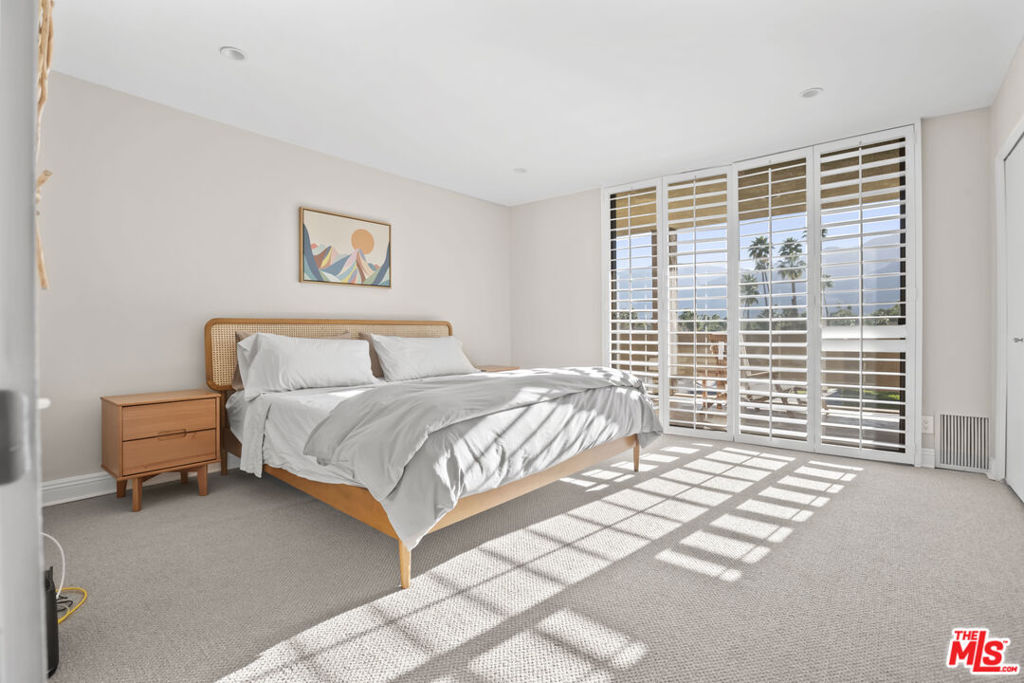 Furnished bedroom with white bedding, plantation shutters, and mountain views.