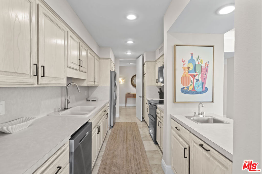 Galley kitchen with white cabinets, stainless steel appliances, and colorful framed artwork.