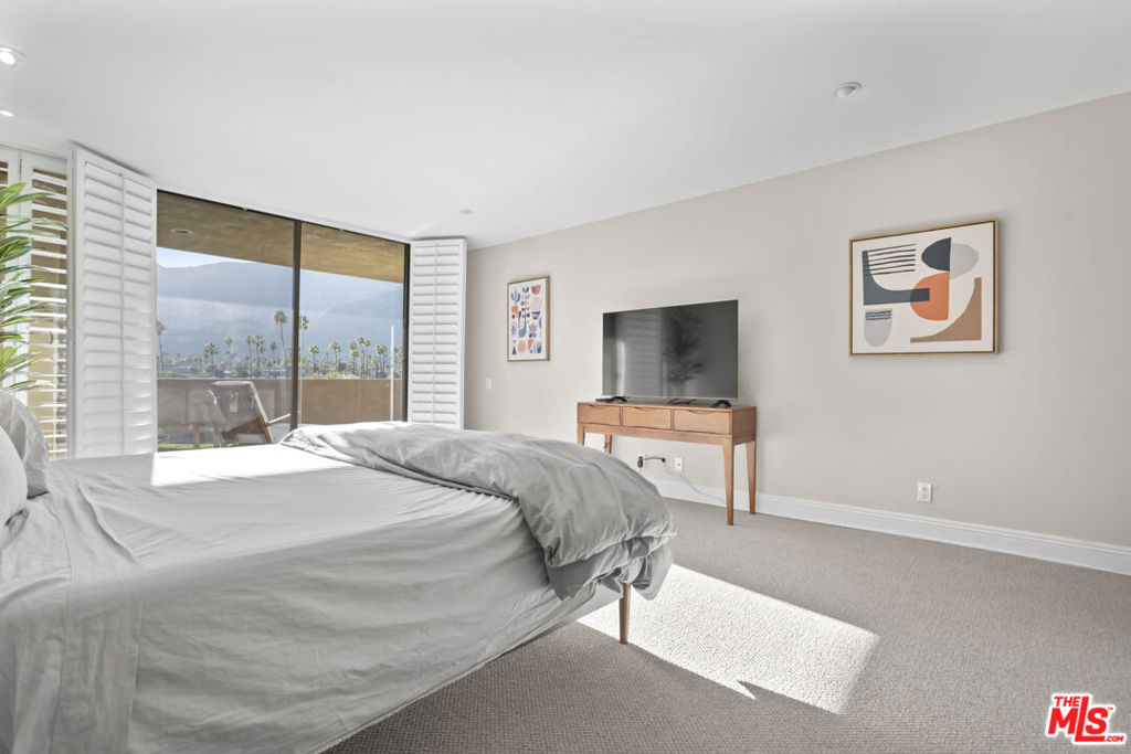 Bright bedroom with a bed, television, and mountain views through a shuttered glass door.