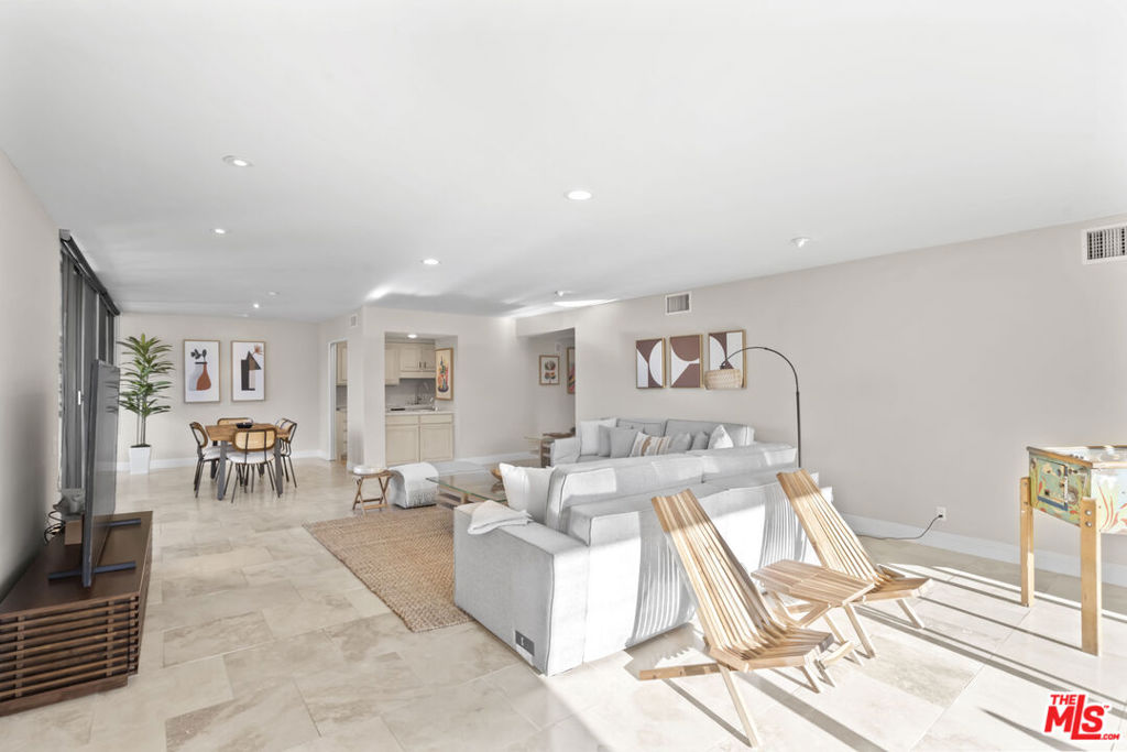 Open-plan living and dining room with white sofas, pale tile floors, and wooden lounge chairs.