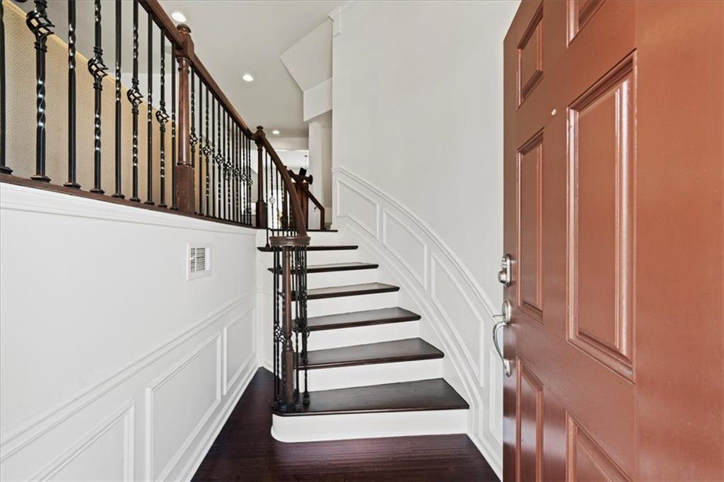 Entry foyer with a dark wood staircase, black iron balusters, and a reddish-brown paneled front door.
