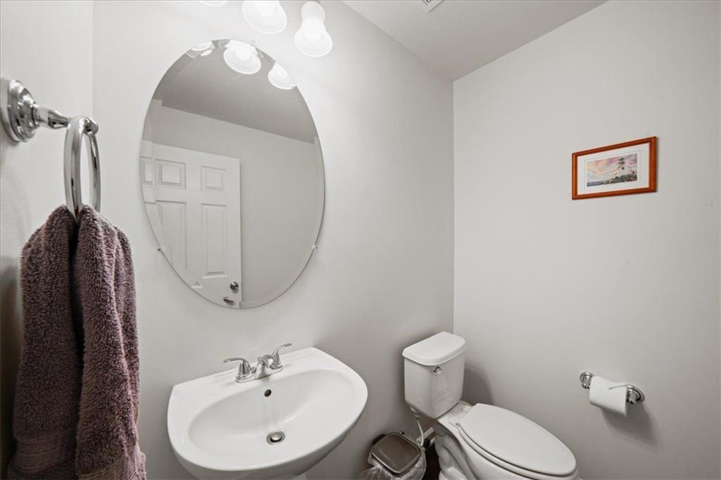 Bathroom with a white sink beneath a large oval mirror and a toilet beside it.