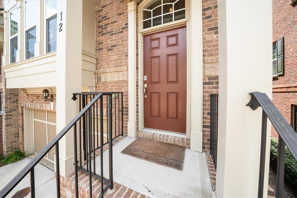 Brick home entrance with a reddish-brown paneled door, arched window, and black railings.