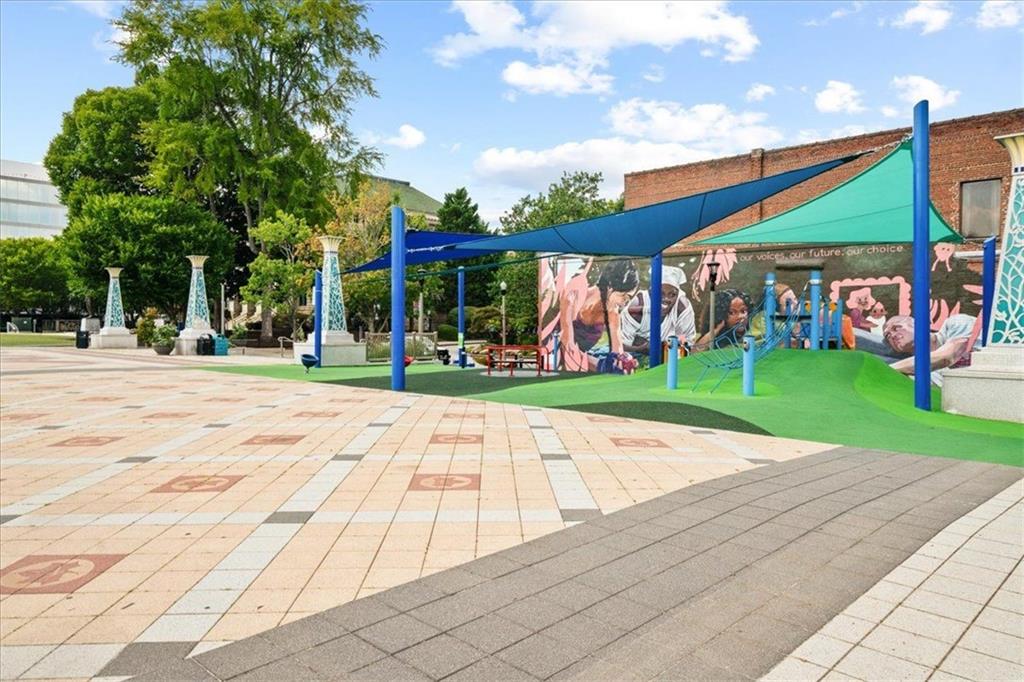 Outdoor playground with blue shade canopies, a green play area, and a colorful mural.
