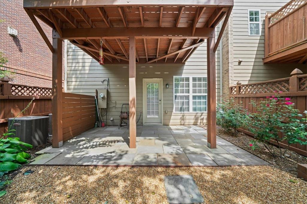 Rear patio beneath a raised wooden deck, with stone paving, privacy fencing, and flowering shrubs.