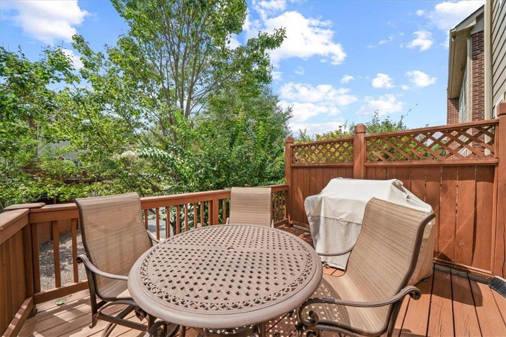 Wooden deck with outdoor dining set, lattice privacy fence, and leafy trees.