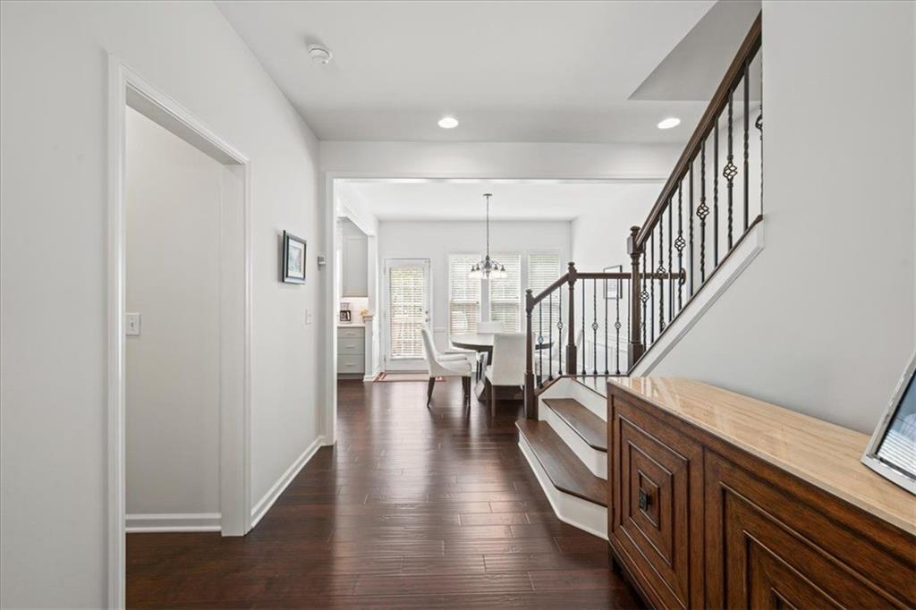 Foyer with dark hardwood floors, a wooden console, and a staircase leading toward a bright dining area.