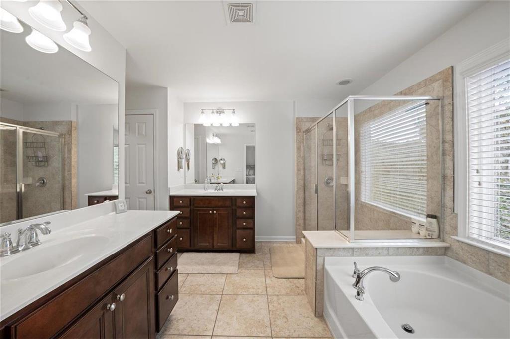 Bathroom with dark wood double vanities, glass-enclosed shower, and corner soaking tub beside windows.