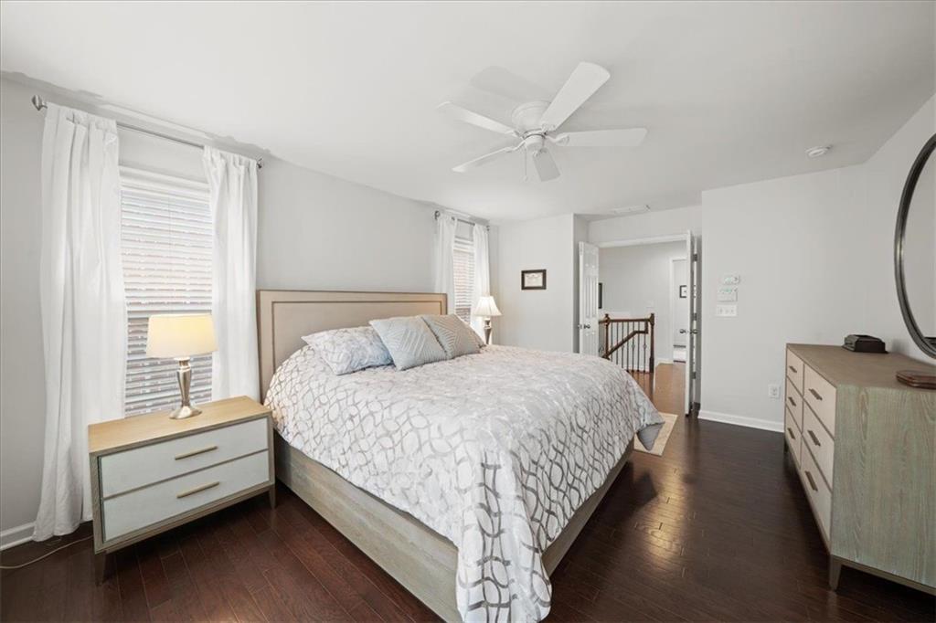 Bedroom with a large bed, patterned white bedding, dark wood floors, and a ceiling fan.