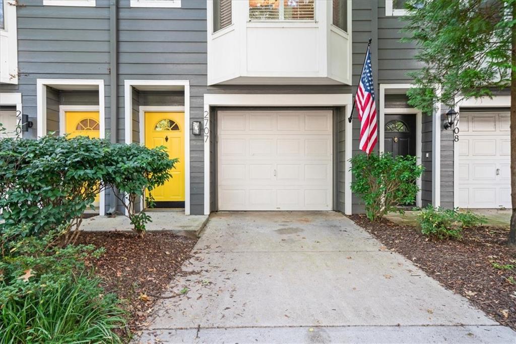Gray-sided attached home with a white garage, yellow entry door, and American flag.