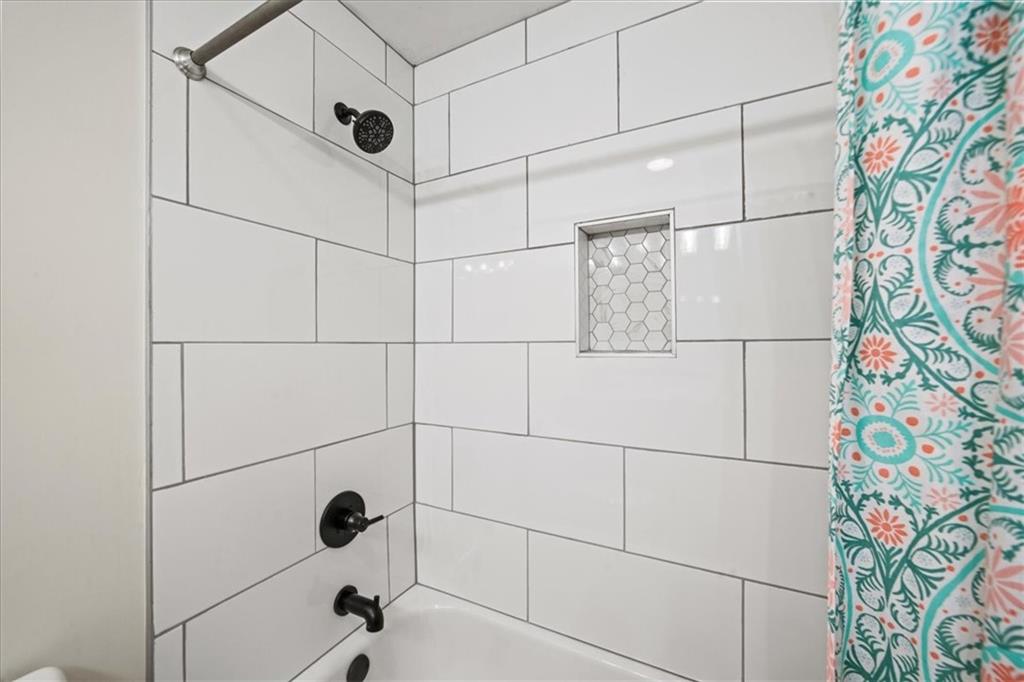 Bathroom tub and shower with white subway tile, a hexagonal niche, black fixtures, and a patterned curtain.
