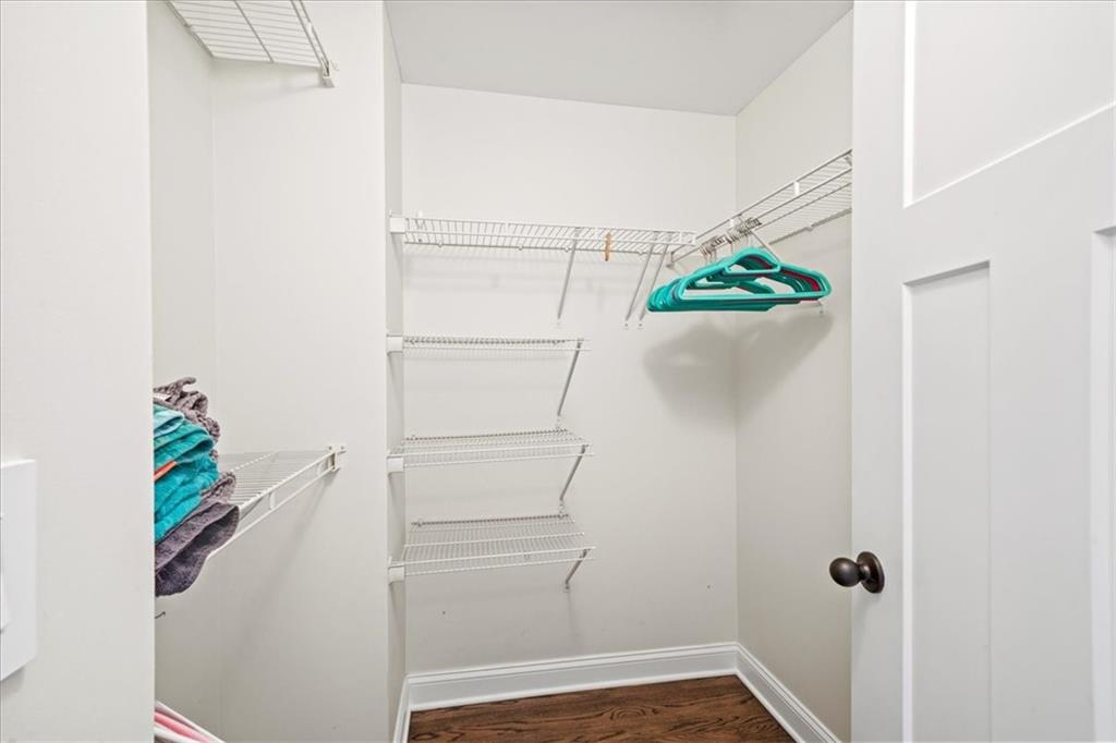 Walk-in closet with wraparound wire shelves, colorful hangers, folded towels, and dark wood flooring.