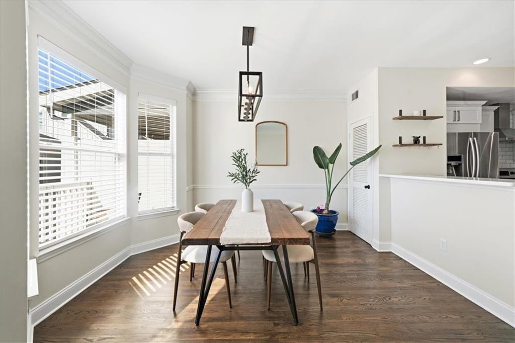 Dining area with a long wooden table beside large windows, opening into the kitchen.