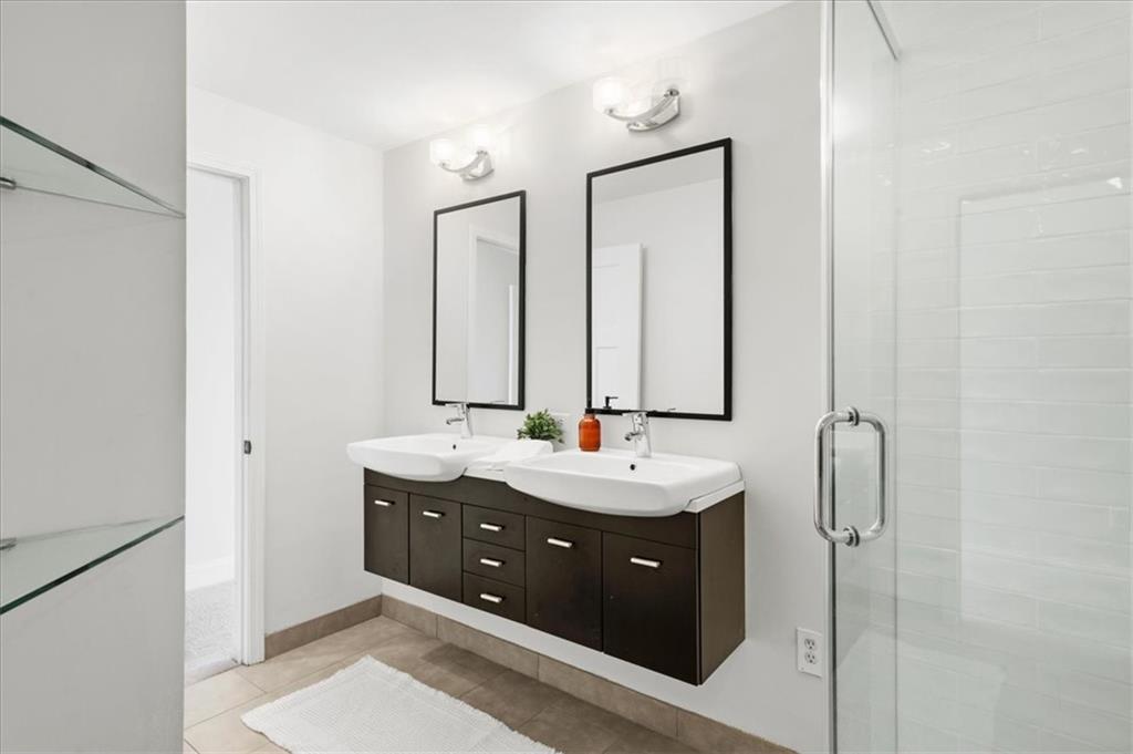 Bathroom with a double-sink vanity, dark cabinets, and a glass-enclosed shower.