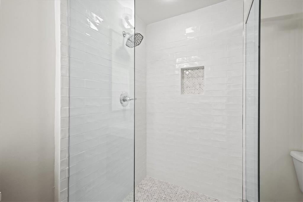Glass-enclosed shower with white subway tile, a rain-style showerhead, and a recessed wall niche.
