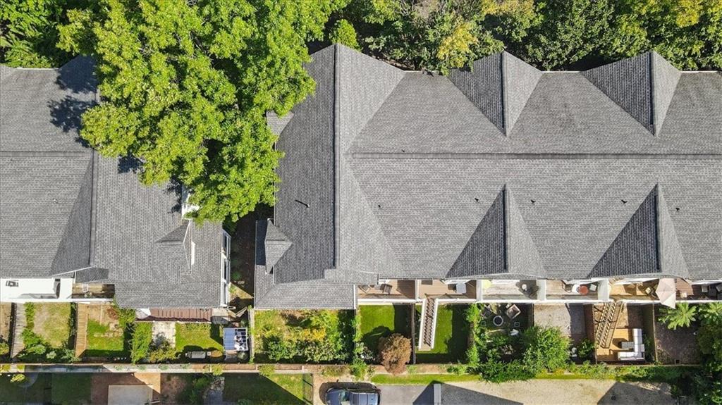Aerial view of attached townhomes with gray roofs, landscaped fenced yards, and mature trees.