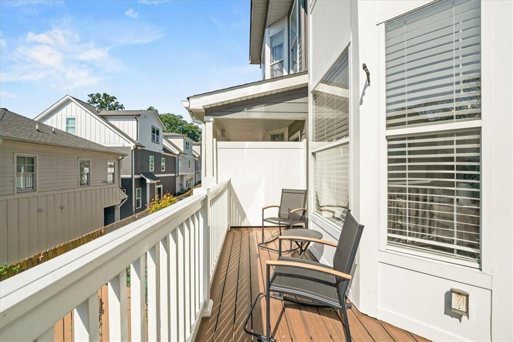 Narrow wooden balcony with white railings and two chairs overlooking neighboring townhouses.
