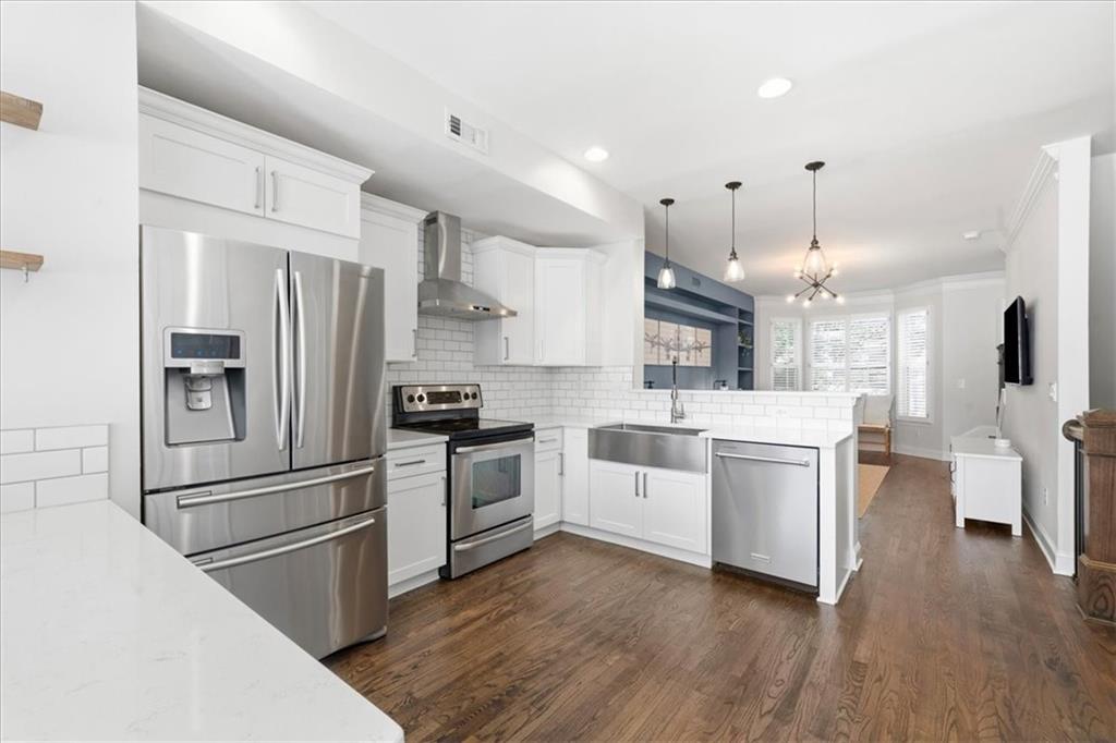 Open-plan kitchen with white cabinets, stainless steel appliances, farmhouse sink, and dark wood floors.