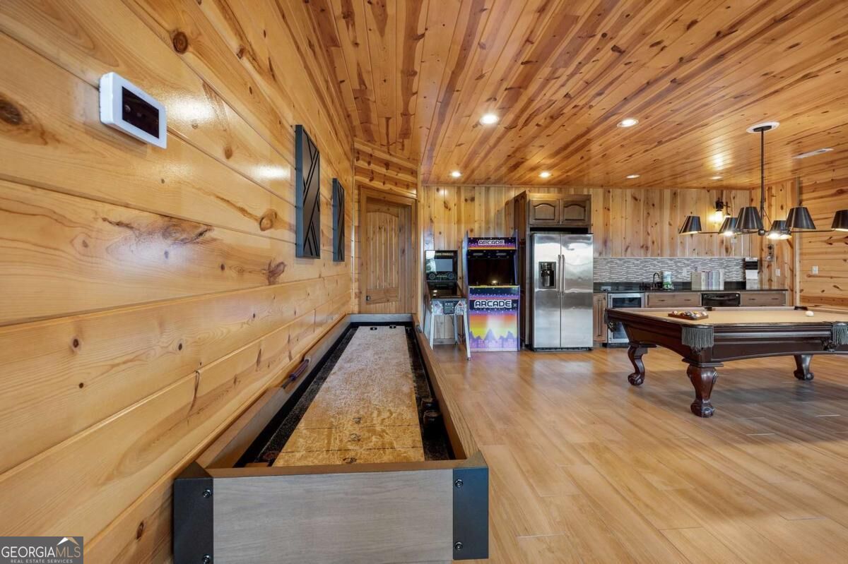 Wood-paneled game room with shuffleboard, arcade cabinets, a pool table, and a compact kitchen.