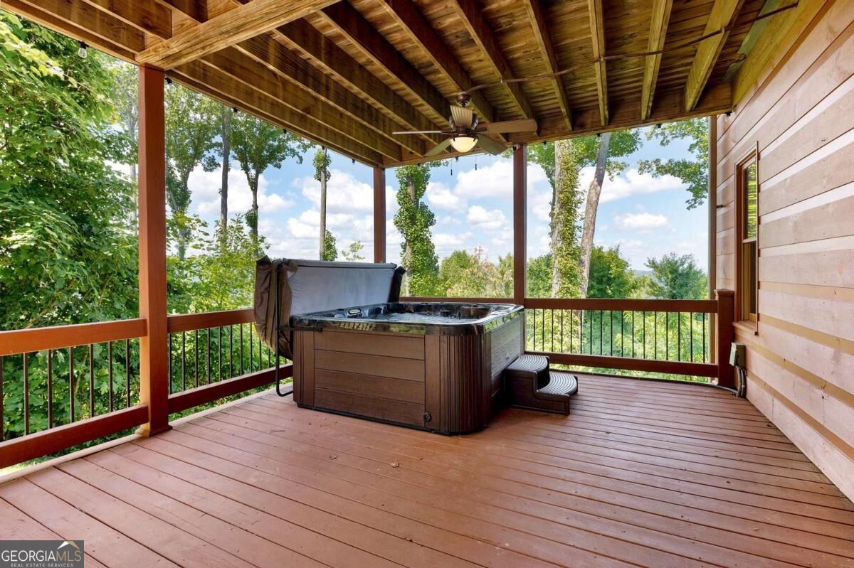 Covered wooden deck with a hot tub and wooded views.