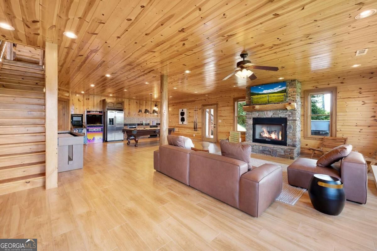 Open-plan living room with a stone fireplace, leather seating, and knotty-pine walls and ceiling.