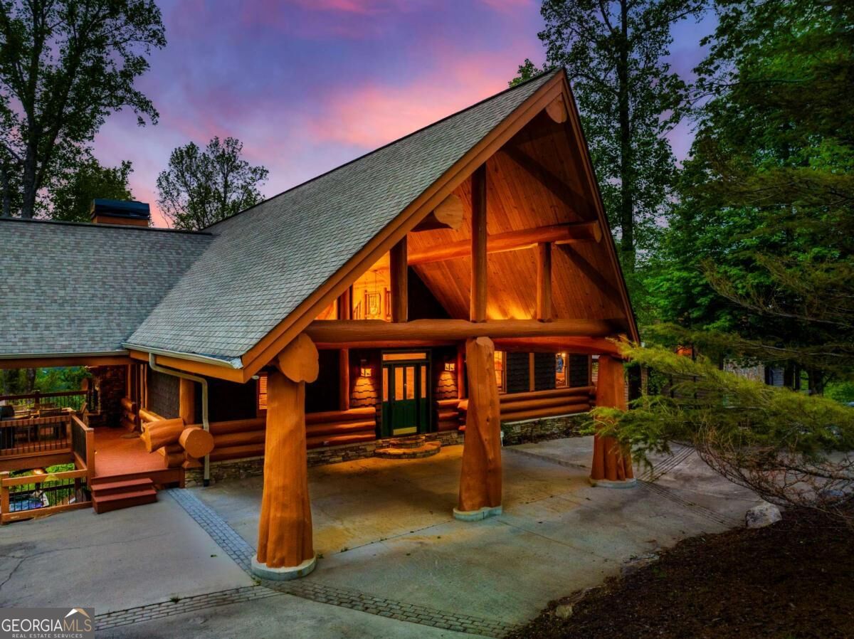 Log cabin home with a tall gabled roof and warmly lit timber porch at dusk.