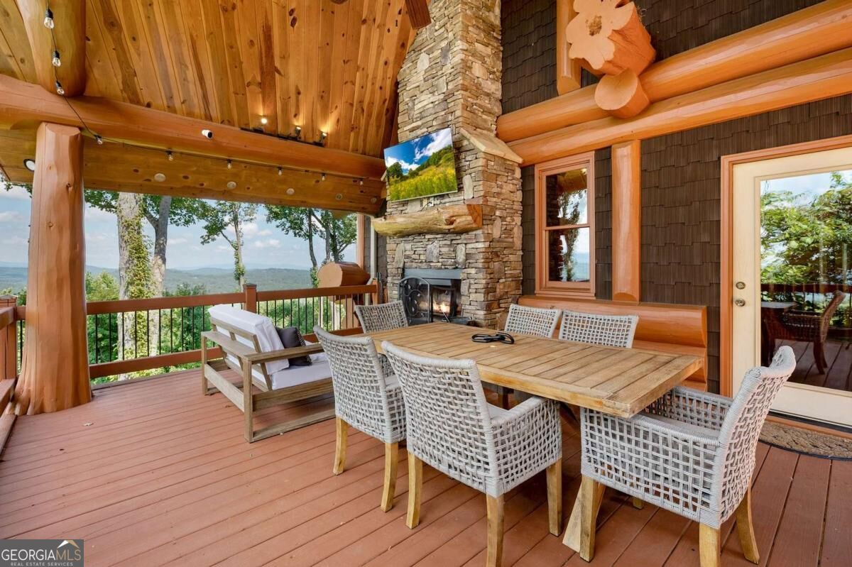 Covered timber deck with stone fireplace, dining set, and mountain views.
