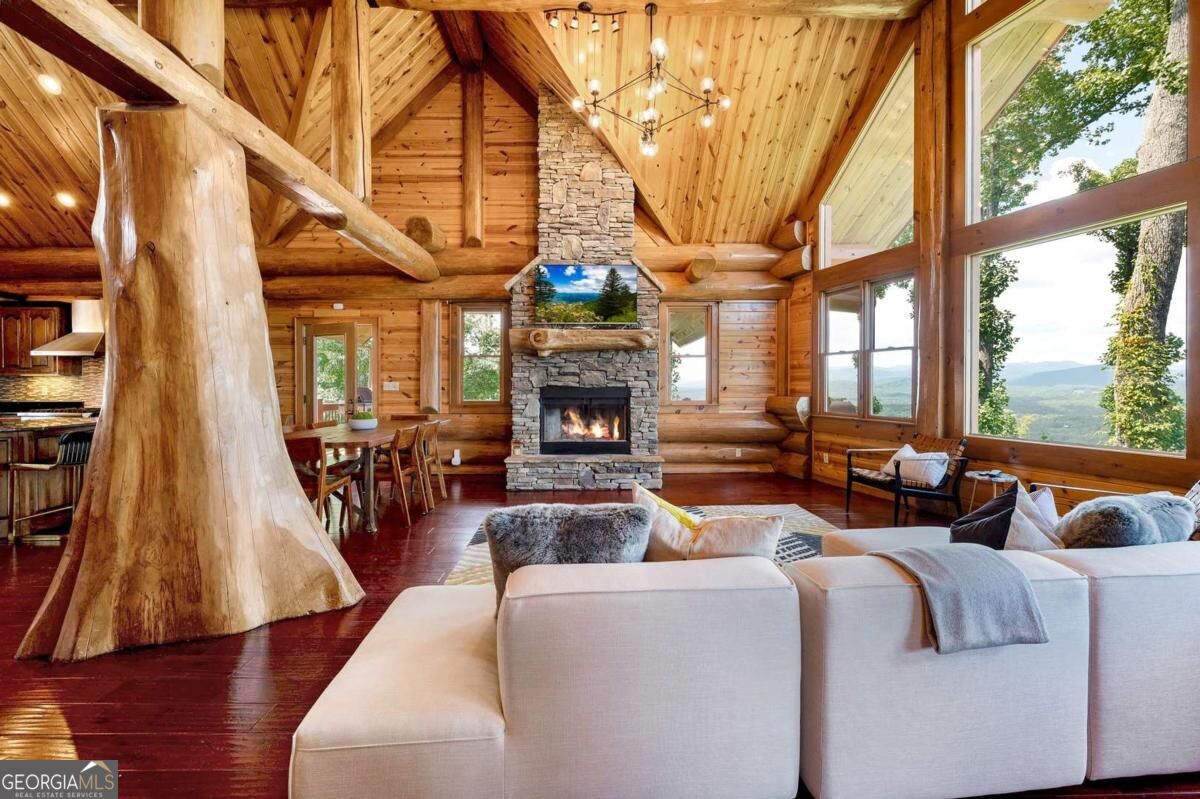 Cabin great room with a stone fireplace, vaulted timber ceiling, and mountain views through tall windows.