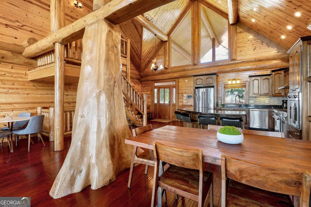 Log cabin kitchen and dining area with vaulted timber ceiling, a massive tree-trunk post, and stainless steel appliances.