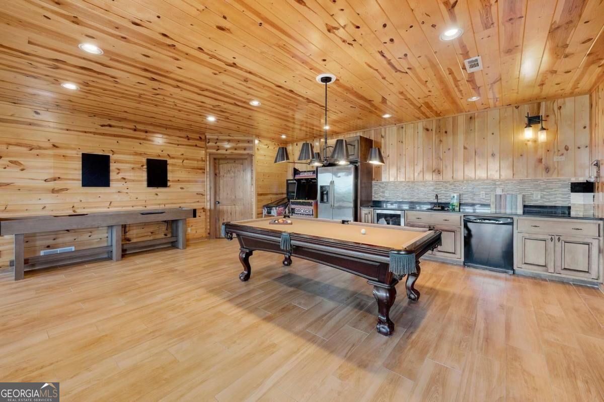 Wood-paneled game room with a pool table, arcade game, and kitchenette.
