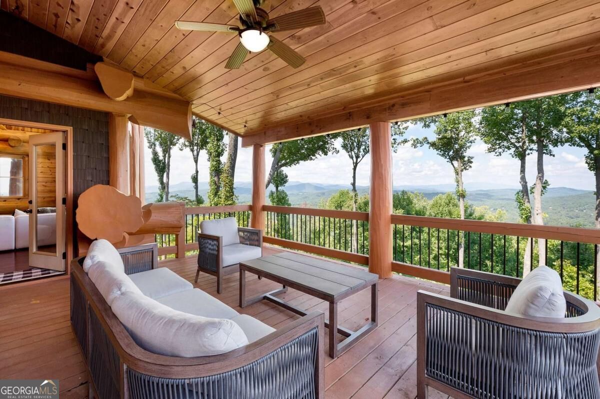 Covered wooden deck with cushioned seating overlooking wooded mountains.