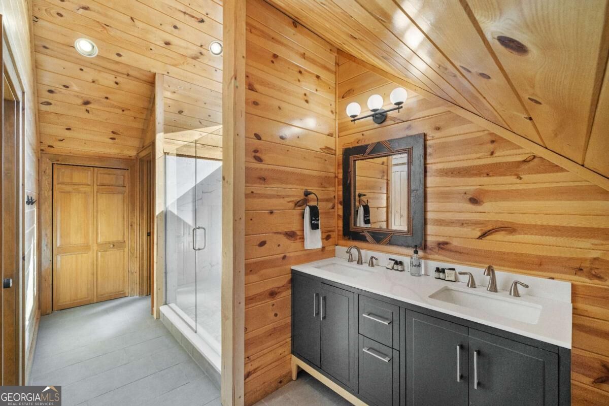Cabin bathroom with a gray double vanity, glass shower, and knotty-pine walls.