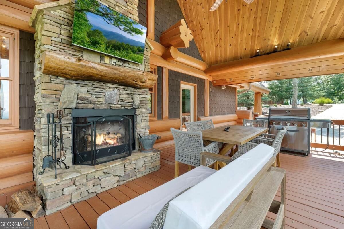 Covered patio with a stone fireplace, wood ceiling, dining table, and stainless steel grill.