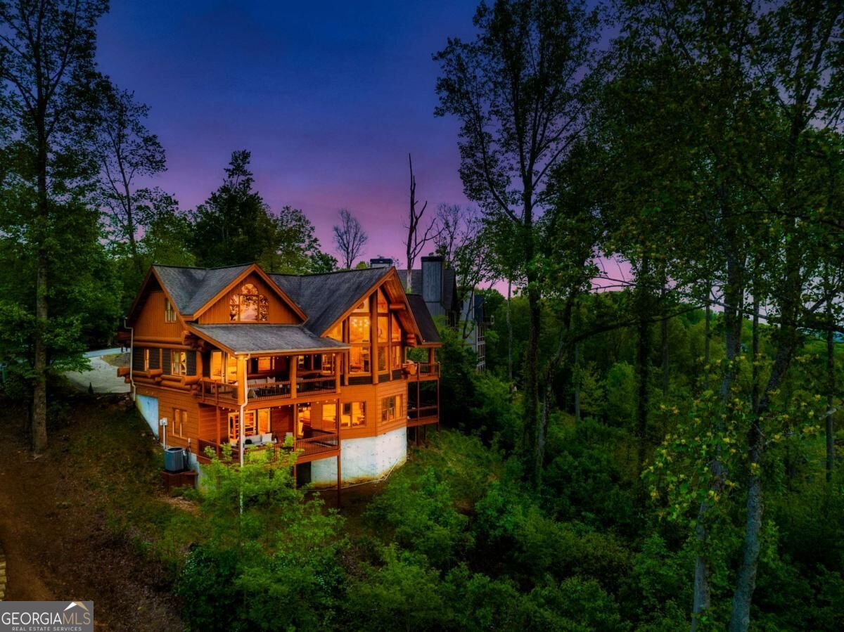 Wooded log cabin with multiple decks glowing warmly at dusk.