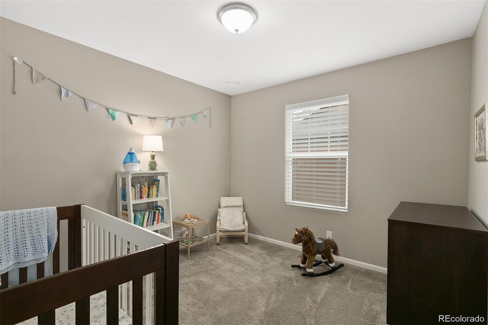 Nursery with a dark wood crib, colorful bunting, and a rocking horse on gray carpet.