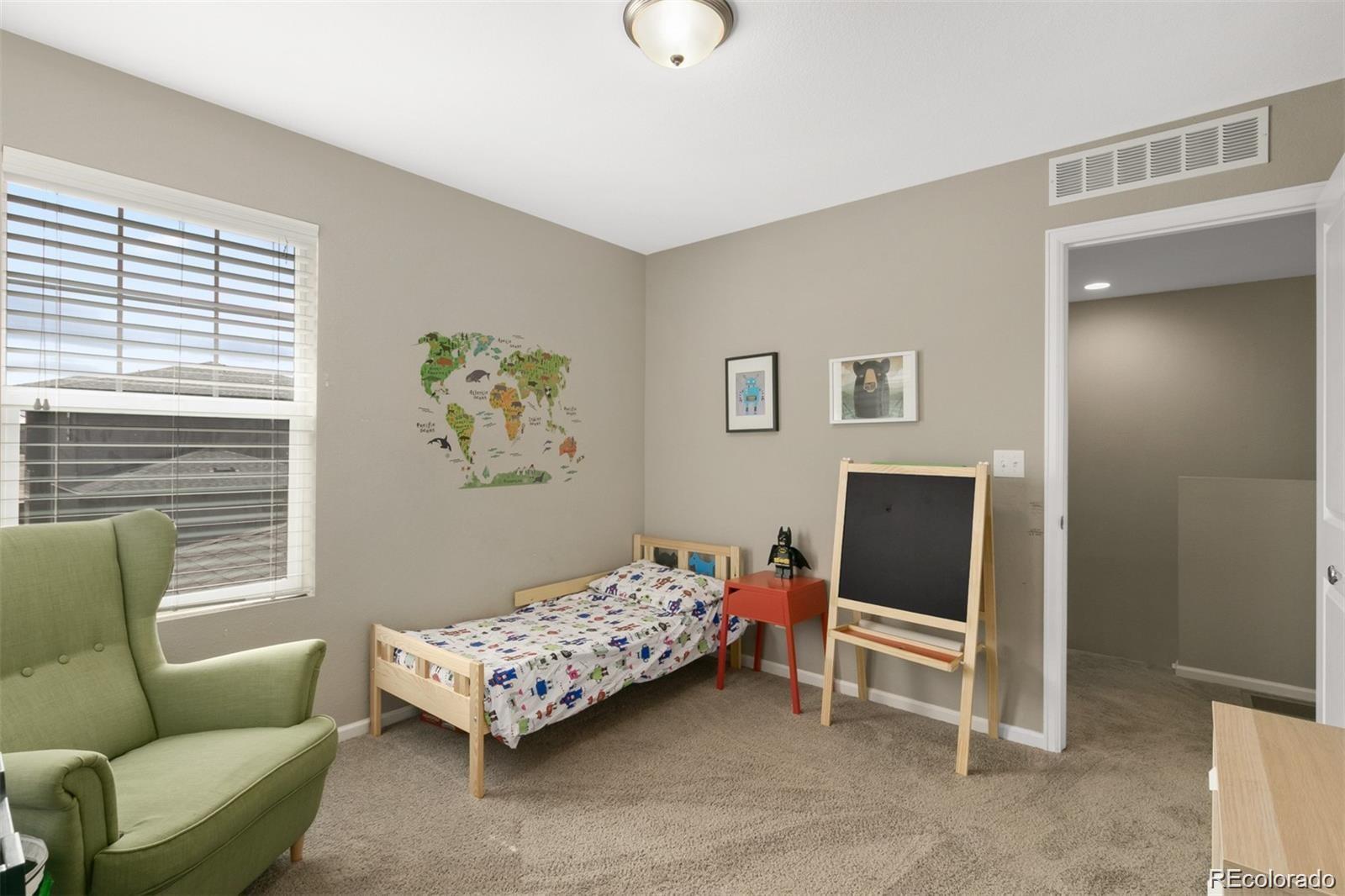 Furnished child’s bedroom with a single bed, green chair, and world map wall decal.